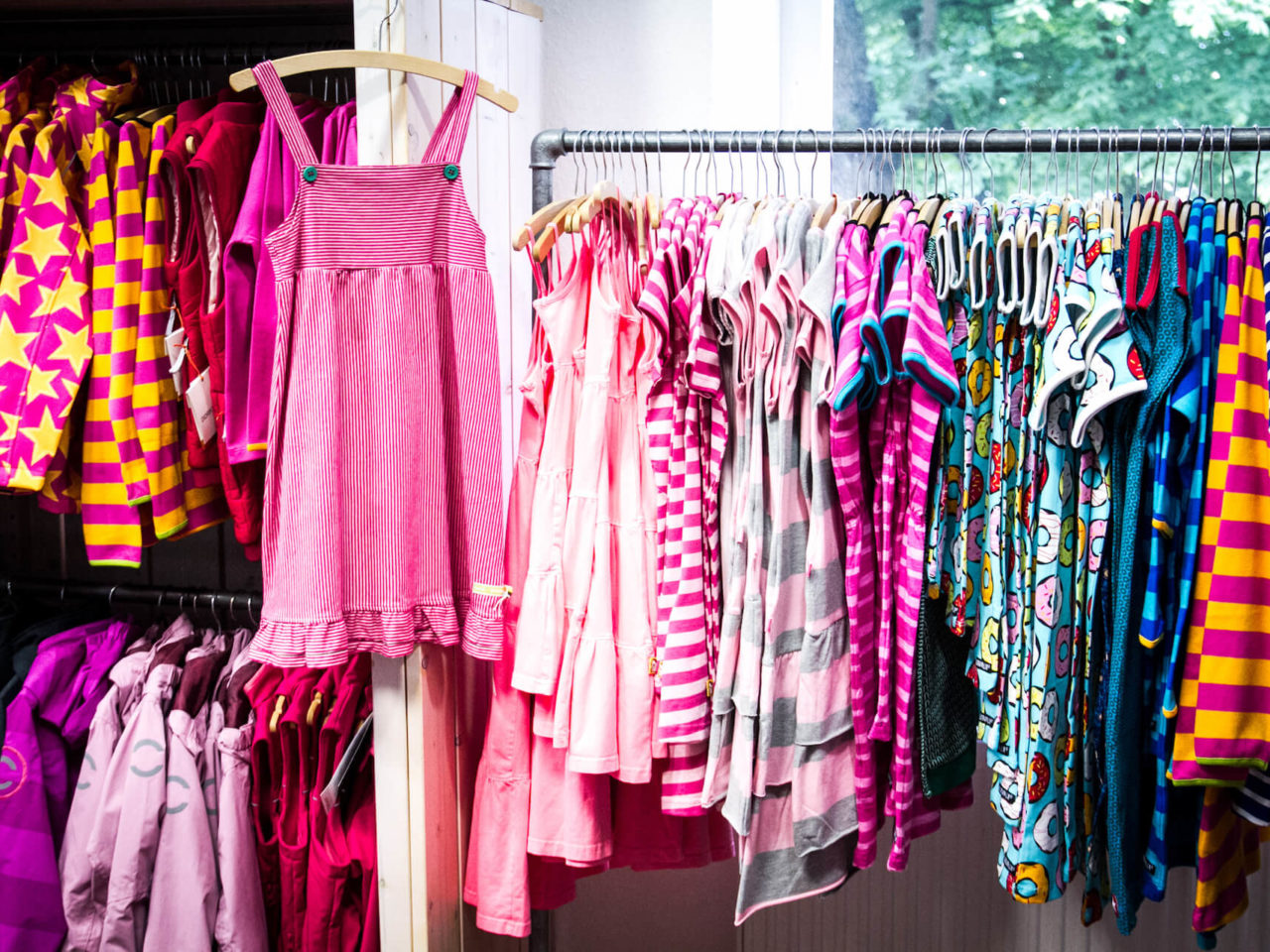 Fröhlich, bunte Mädchenkleider in pink, rosa, gelb und anderen Farben hängen an einer Stange im Elli & Mai in Lüneburg