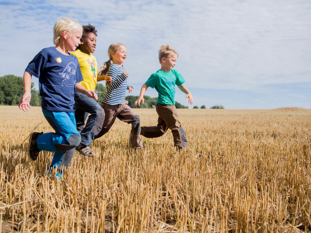 Drei Jungs und ein Mädchen in bunter Kindermode von Elli & Mai laufen üebr ein Feld